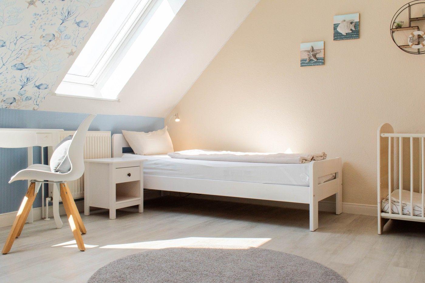 Ein Schlafzimmer mit Dachschrägen, Bett, Kinderbett und Schreibtisch unter Dachfenster.