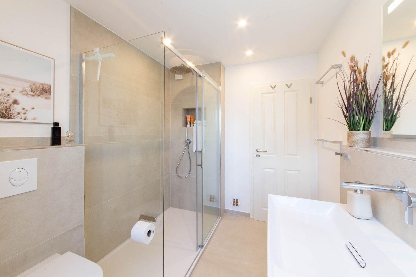Badezimmer mit Dusche, Waschbecken und Toilette. Modern eingerichtet mit Glaswand und Pflanze.