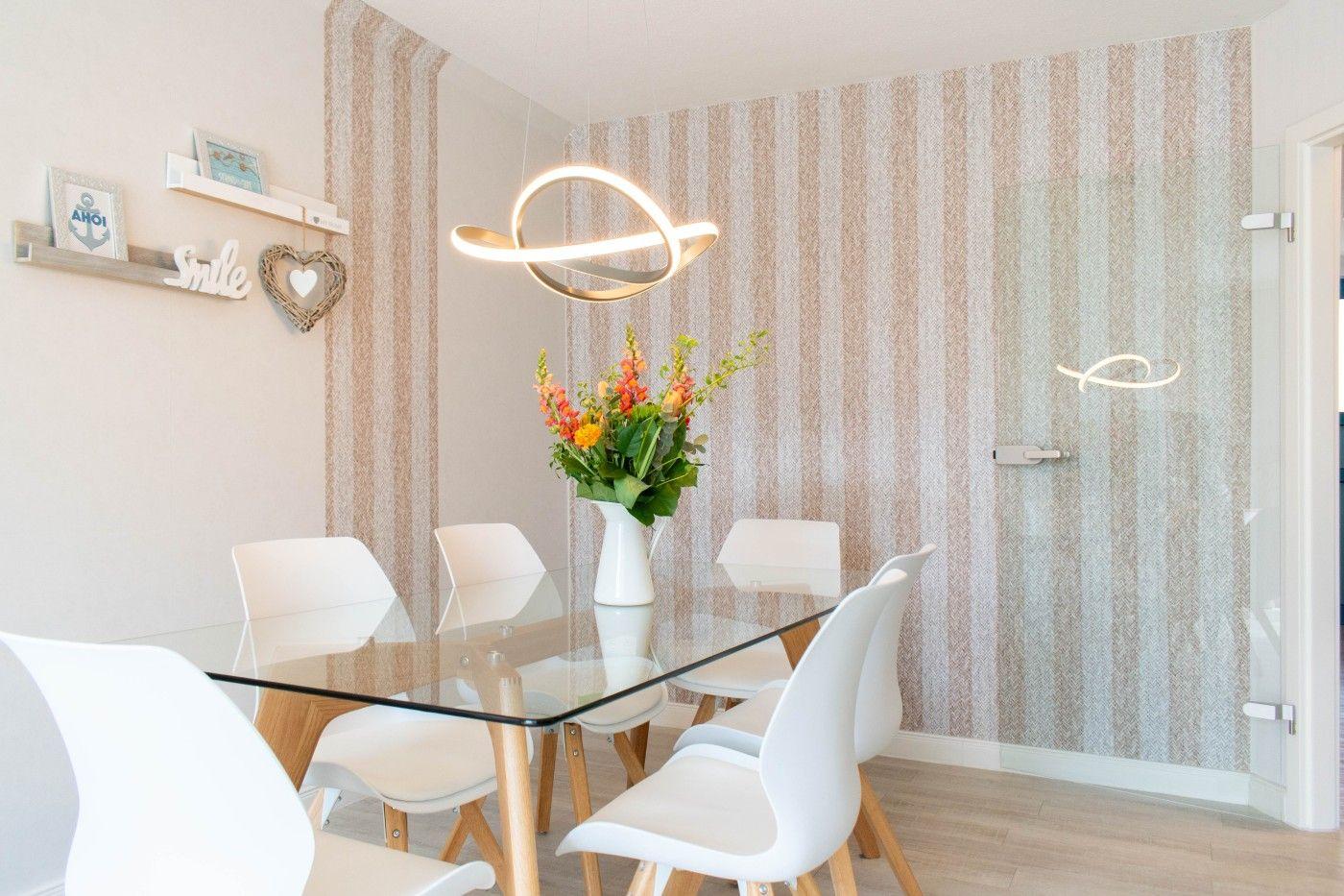 Essbereich mit Glas-tisch, weißen Stühlen und Blumenarrangement. Streifenwand und moderne Lampe.