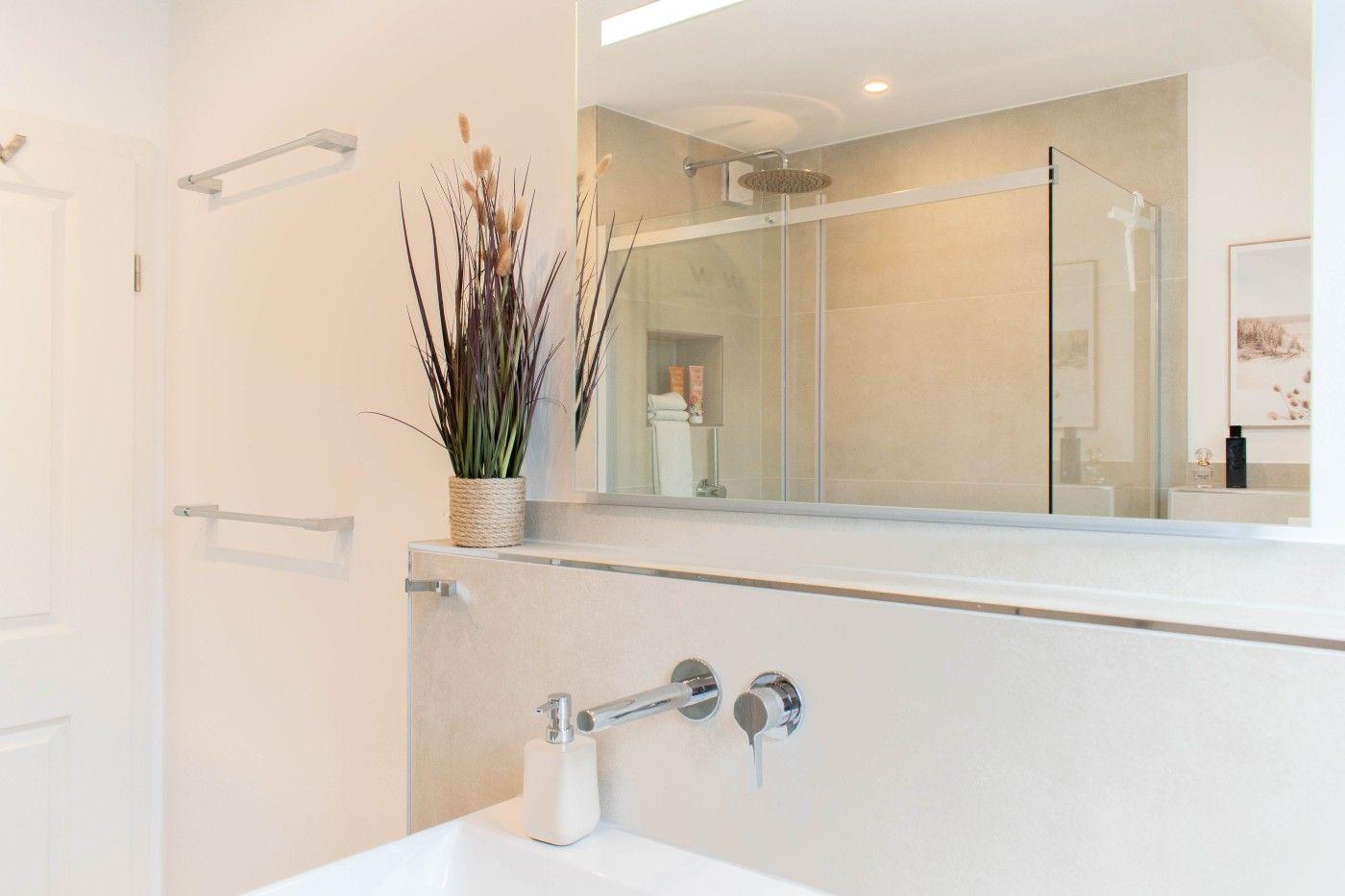 Bad mit Waschbecken, Spiegel und Dusche mit Glaswand.