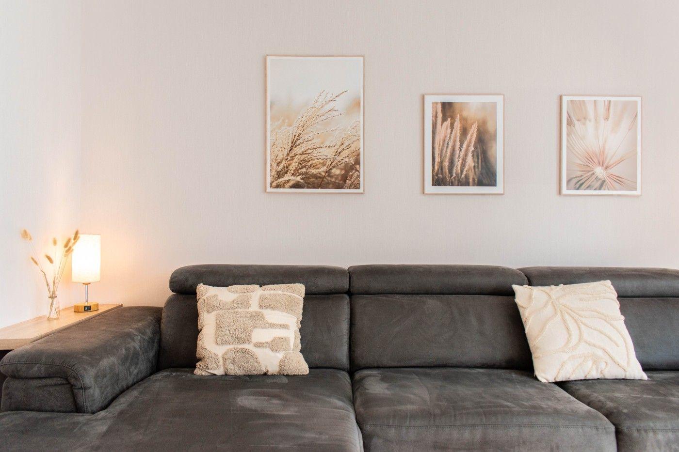 Ein grauer Sofa mit zwei Kissen und drei Wandbildern über dem Sofa.