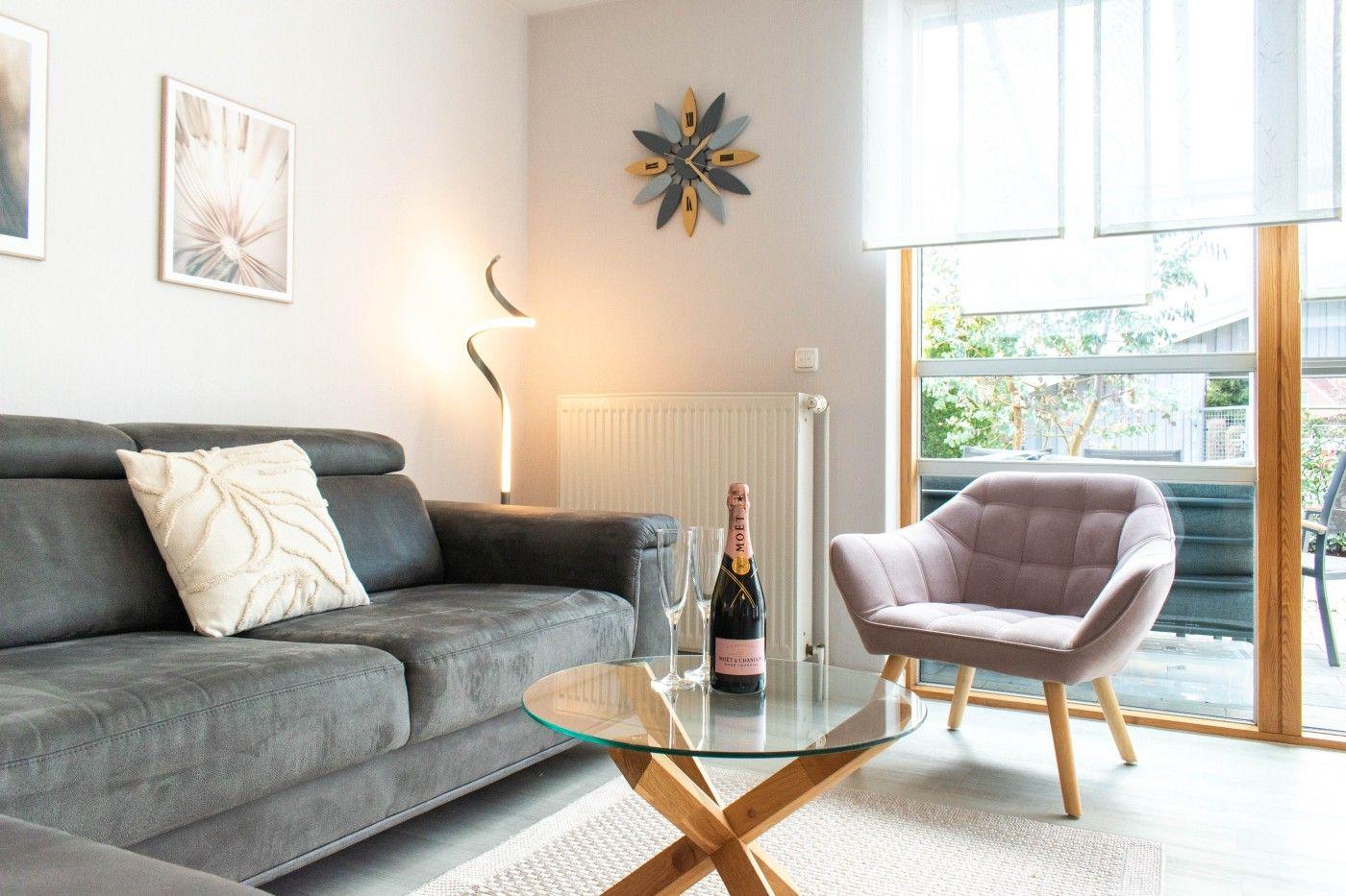 Ein Wohnzimmer mit grauem Sofa, rosa Sessel und Glas-Tisch mit Champagner.
