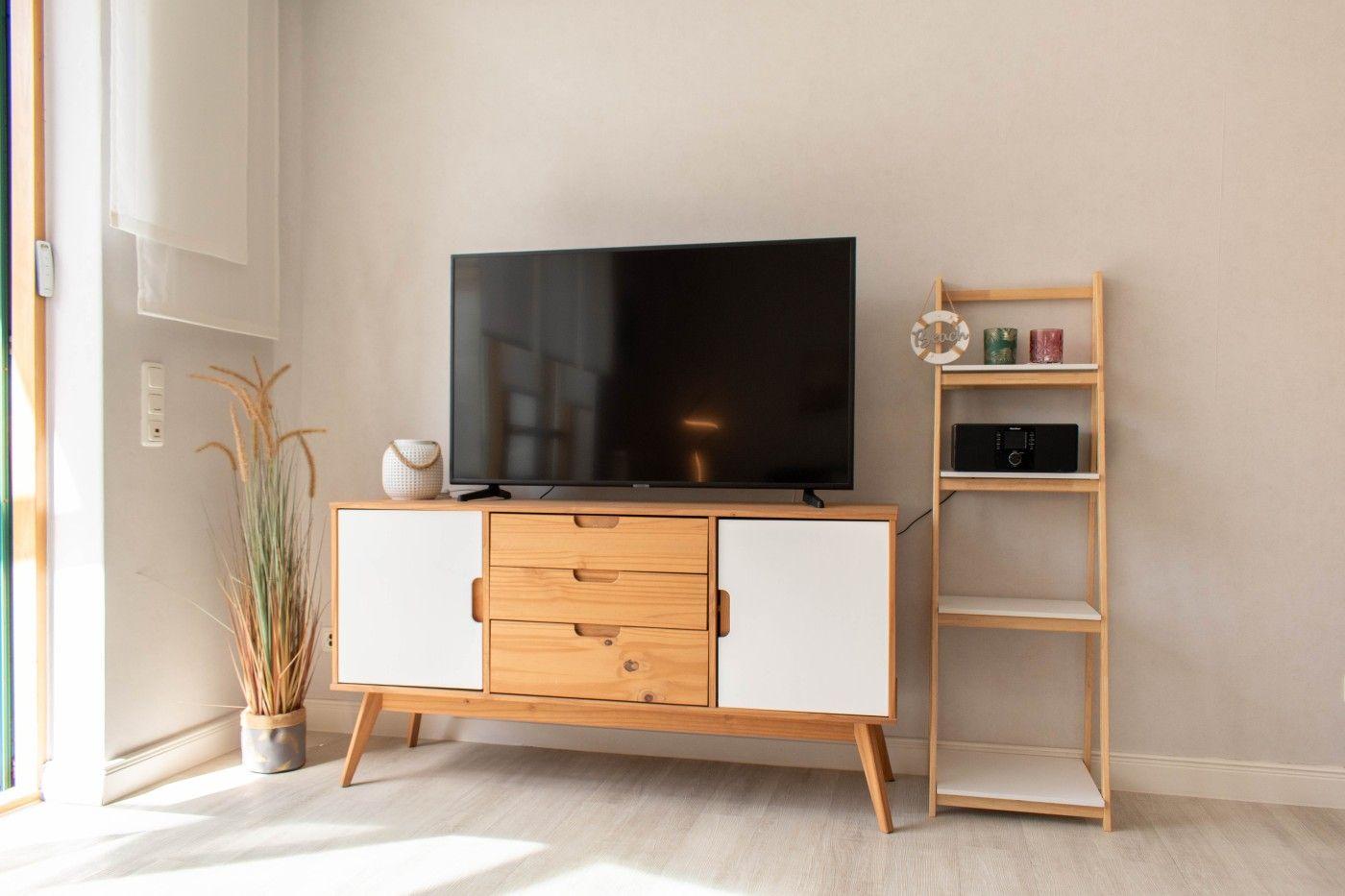 TV auf Holz-Schrank mit weißen Türen. Nebenher steht ein Bücherregal mit Geräten.