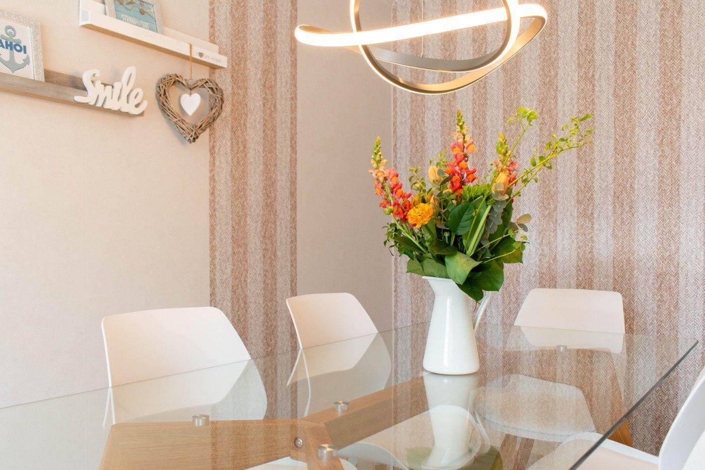 Esstisch mit vier Stühlen, Blumen und moderner Deckenleuchte.