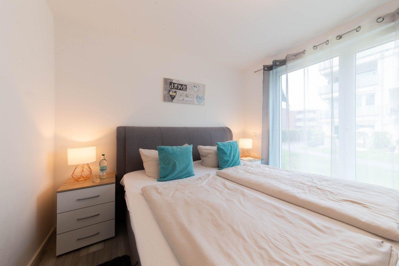 Schlafzimmer mit Doppelbett, Nachttisch und großem Fenster.