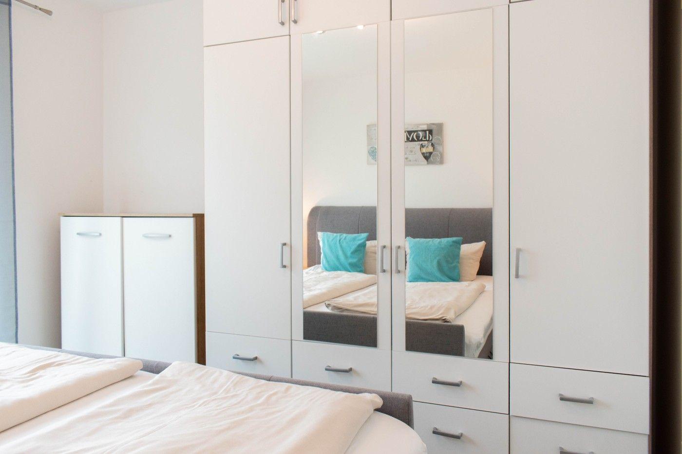 Schlafzimmer mit weißem Schrank und Spiegeltüren, Bett mit Kissen und Decke.