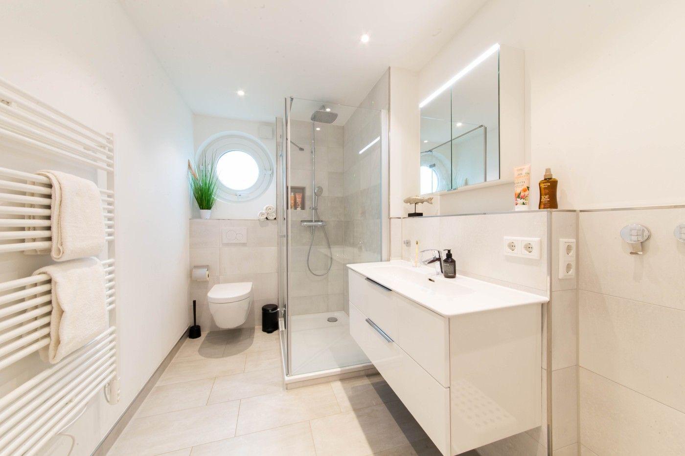 Badezimmer mit Dusche, Waschbecken und Toilette. Rundes Fenster und Handtuchheizkörper.