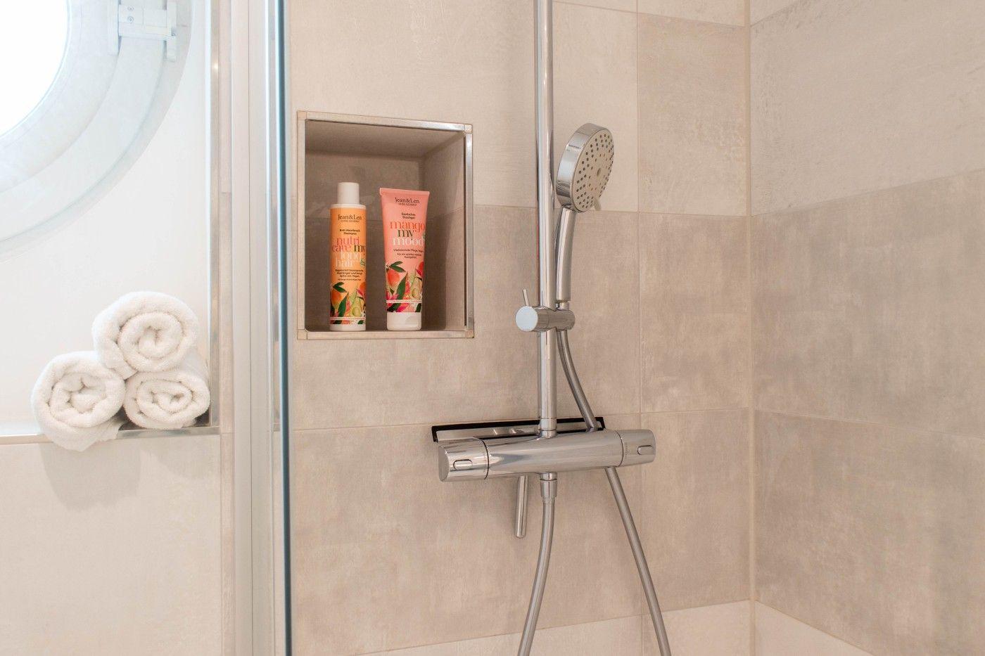 Dusche mit Duschbrause, integriertem Regal und drei gefalteten Handtüchern.