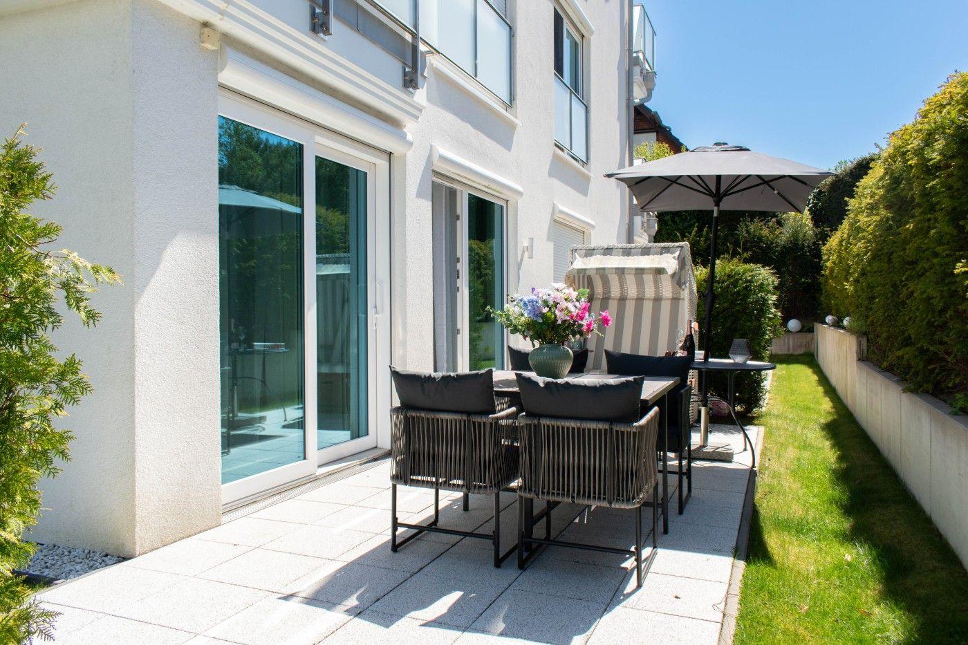 Terrasse mit Tisch, Stühlen und Sonnenschutz neben modernem Haus mit Glasfenstern.