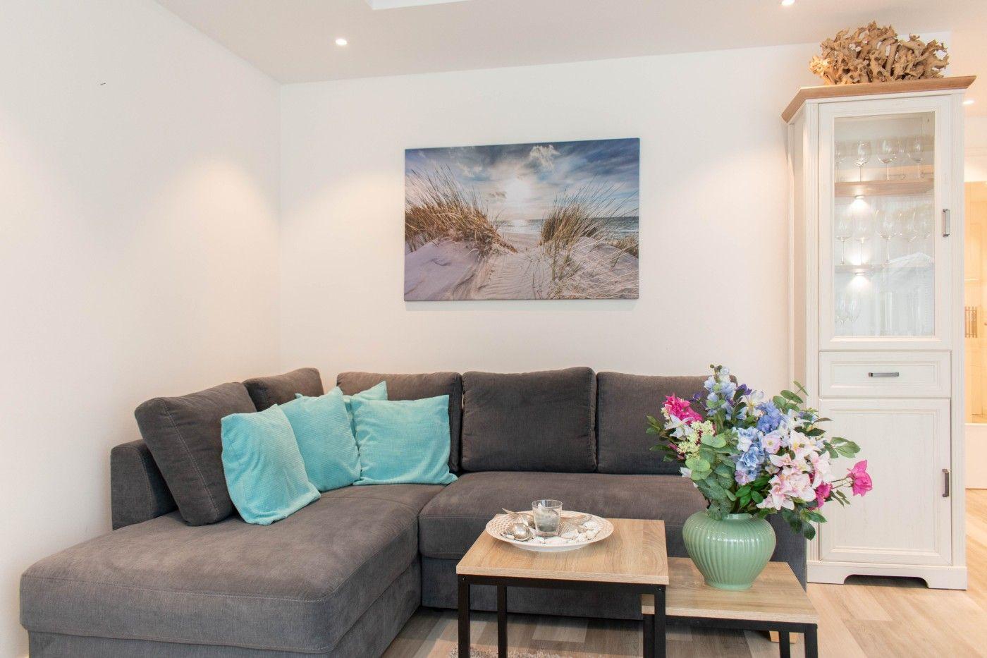 Ein Wohnzimmer mit grauem Sofa, blauen Kissen, Holztisch und Blumenvase.