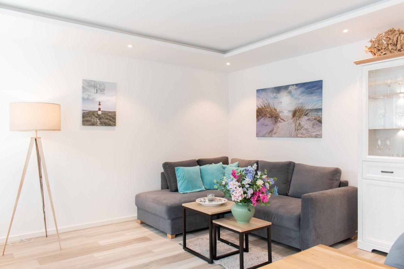 Wohnzimmer mit grauem Sofa, Holztisch und Wandbildern.