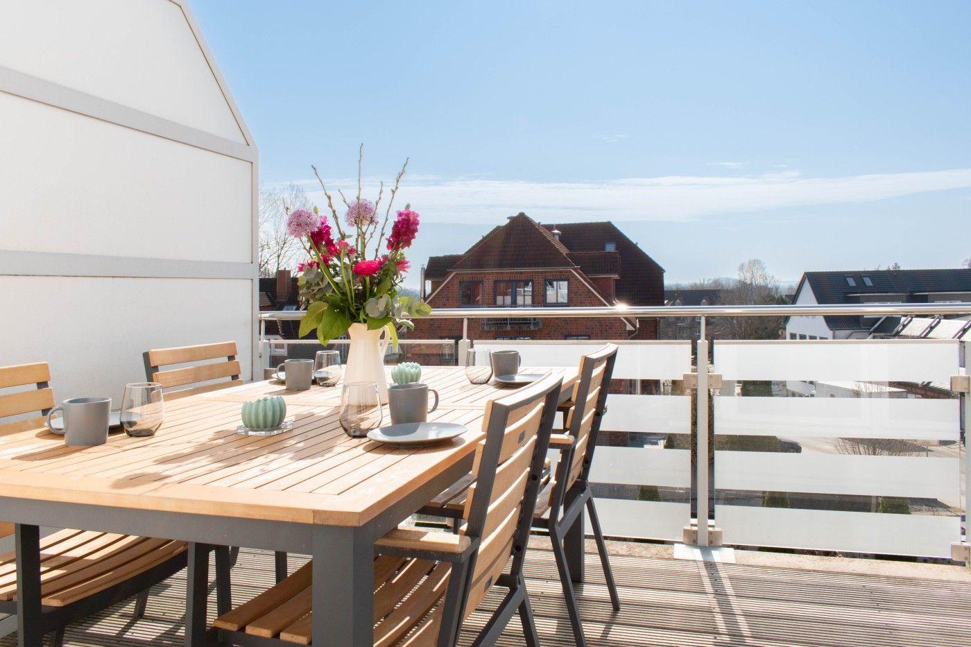 Terrasse mit Tisch, Stühlen und Blumenarrangement. Blick auf Wohnhäuser im Hintergrund.