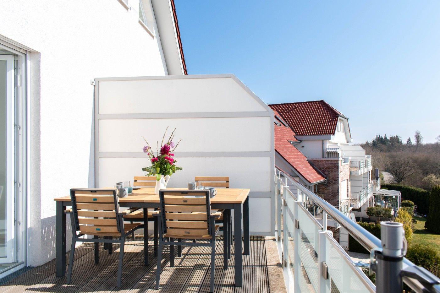 Terrasse mit Tisch, Stühlen und Blumenarrangement. Blick auf Wohnhäuser und Grünflächen.
