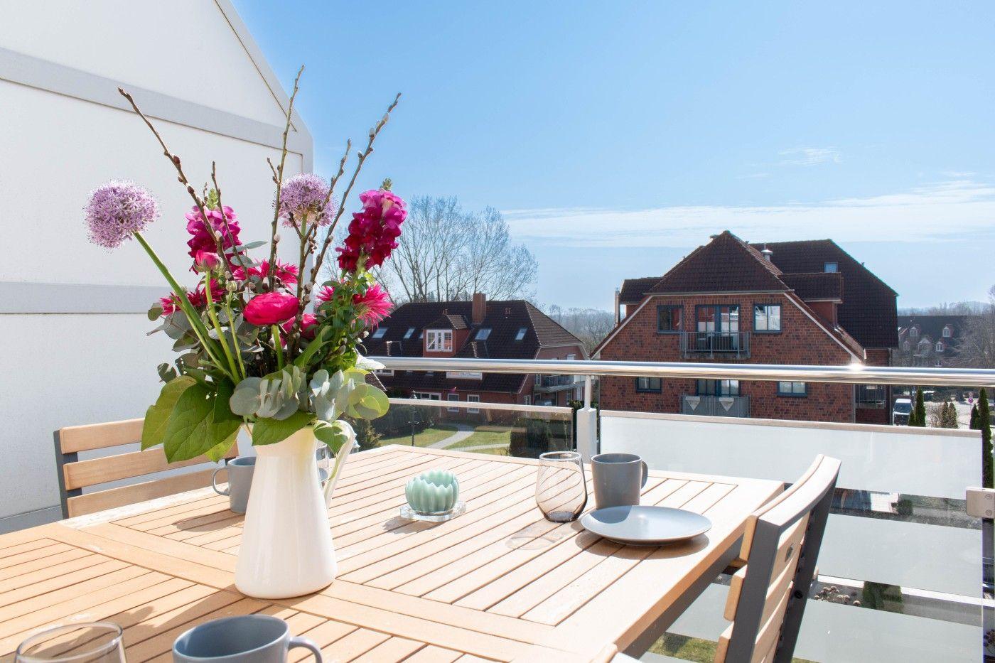 Terrasse mit Tisch, Stühlen und Blumenarrangement. Blick auf Wohnhäuser und Grünflächen.