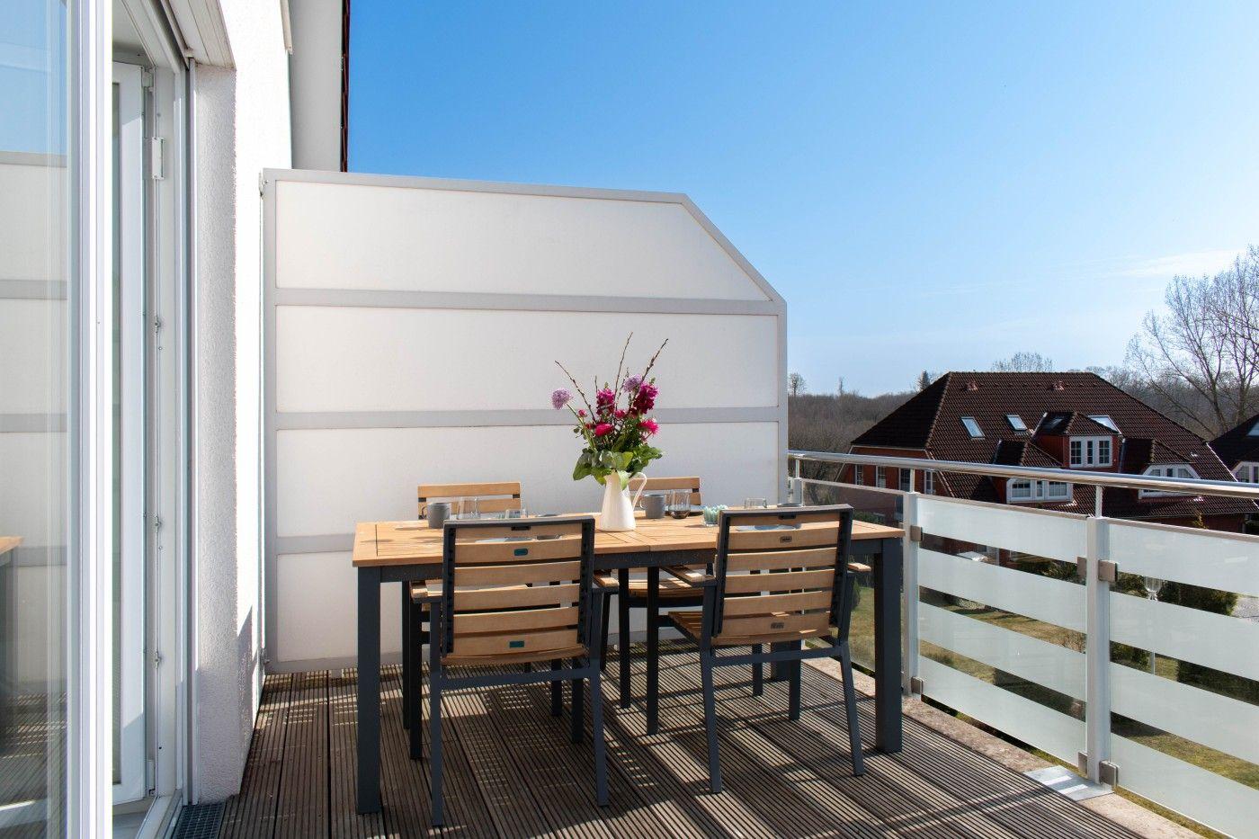 Terrasse mit Holztisch, Stühlen und Blumenvase. Blick auf Dächer und Himmel.