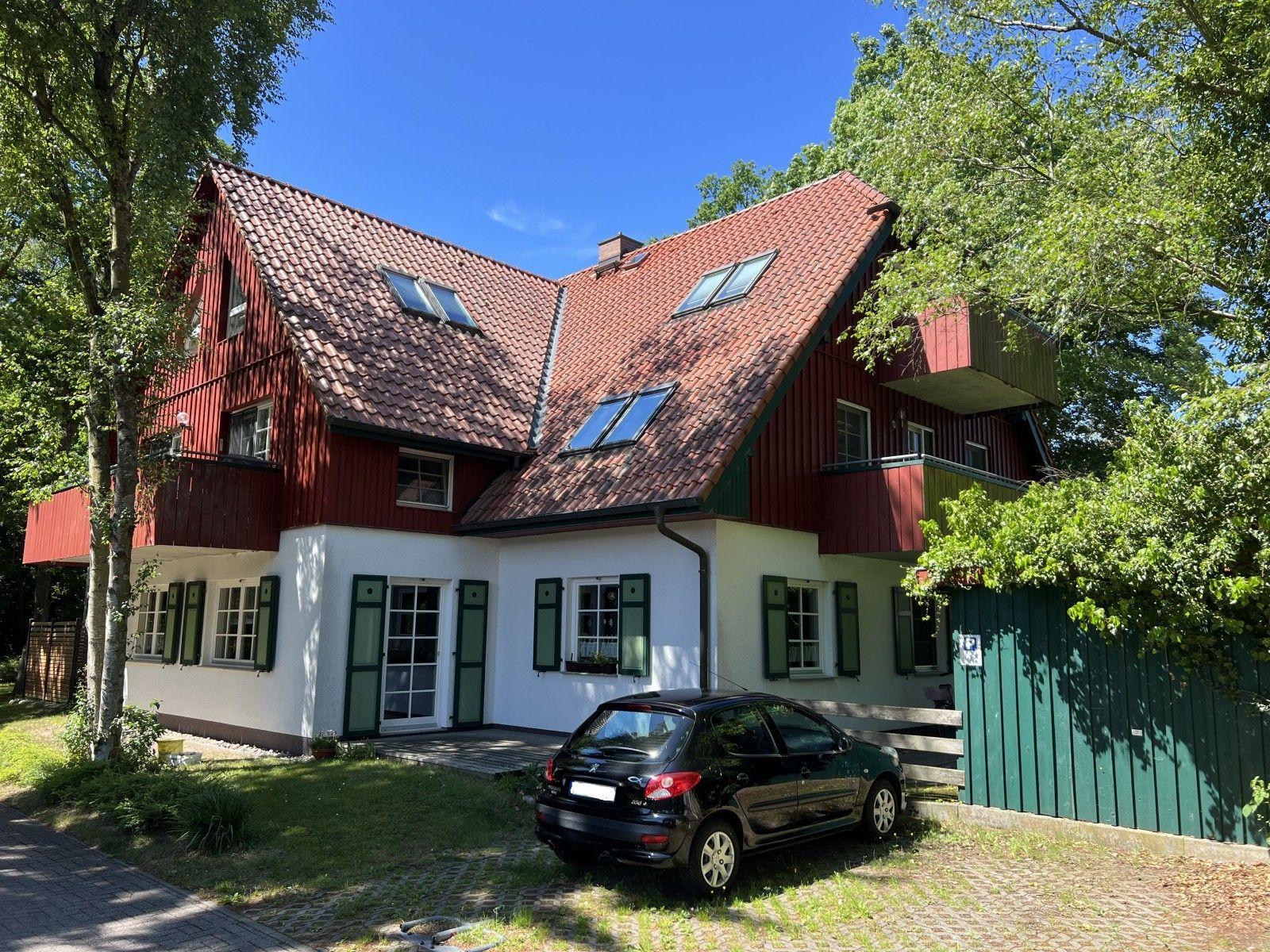 Rotes Holzhaus mit Dachgauben, weißer Sockel, grüne Fensterläden und parkender Wagen.