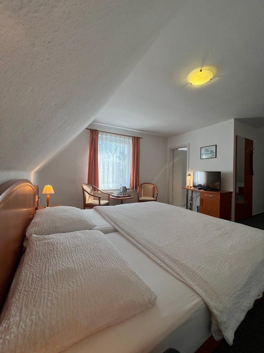 Doppelbett, Fenster mit Vorhängen, zwei Stühle, Fernseher und Schrank.