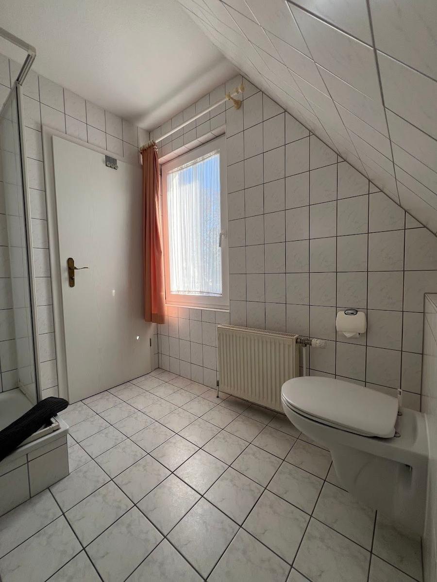 Badezimmer mit Dusche, Toilette und Fenster unter Dachschräge