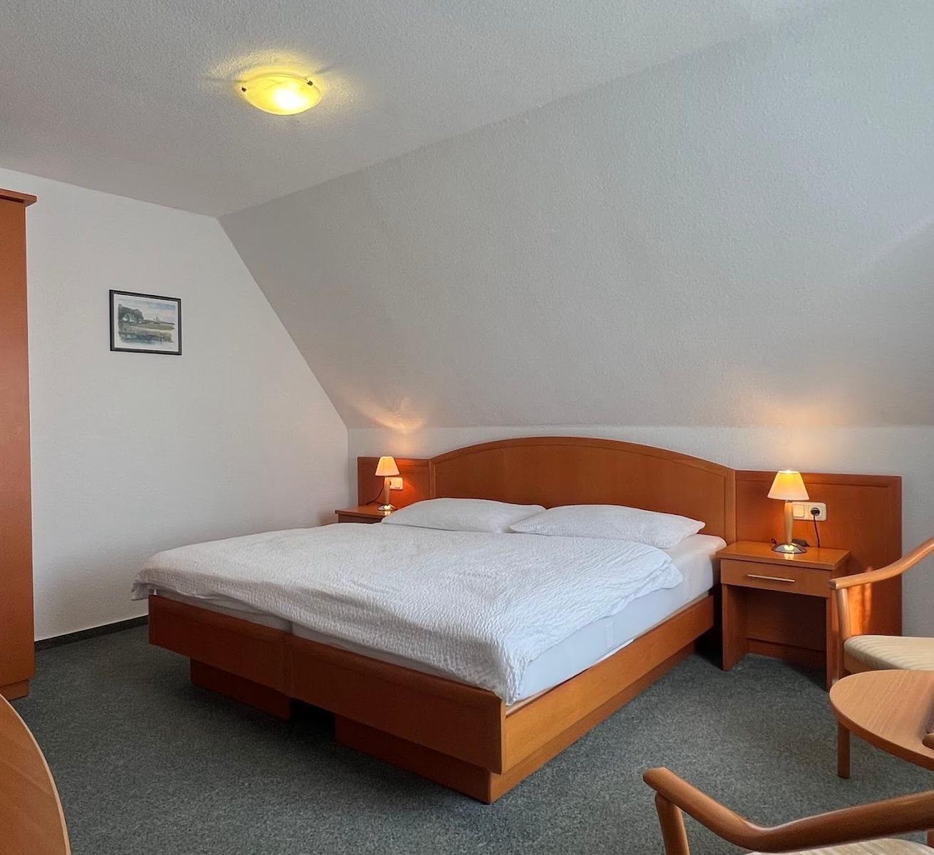 Doppelbett mit Holzrahmen, zwei Nachttische mit Lampen und Stuhl im Zimmer.
