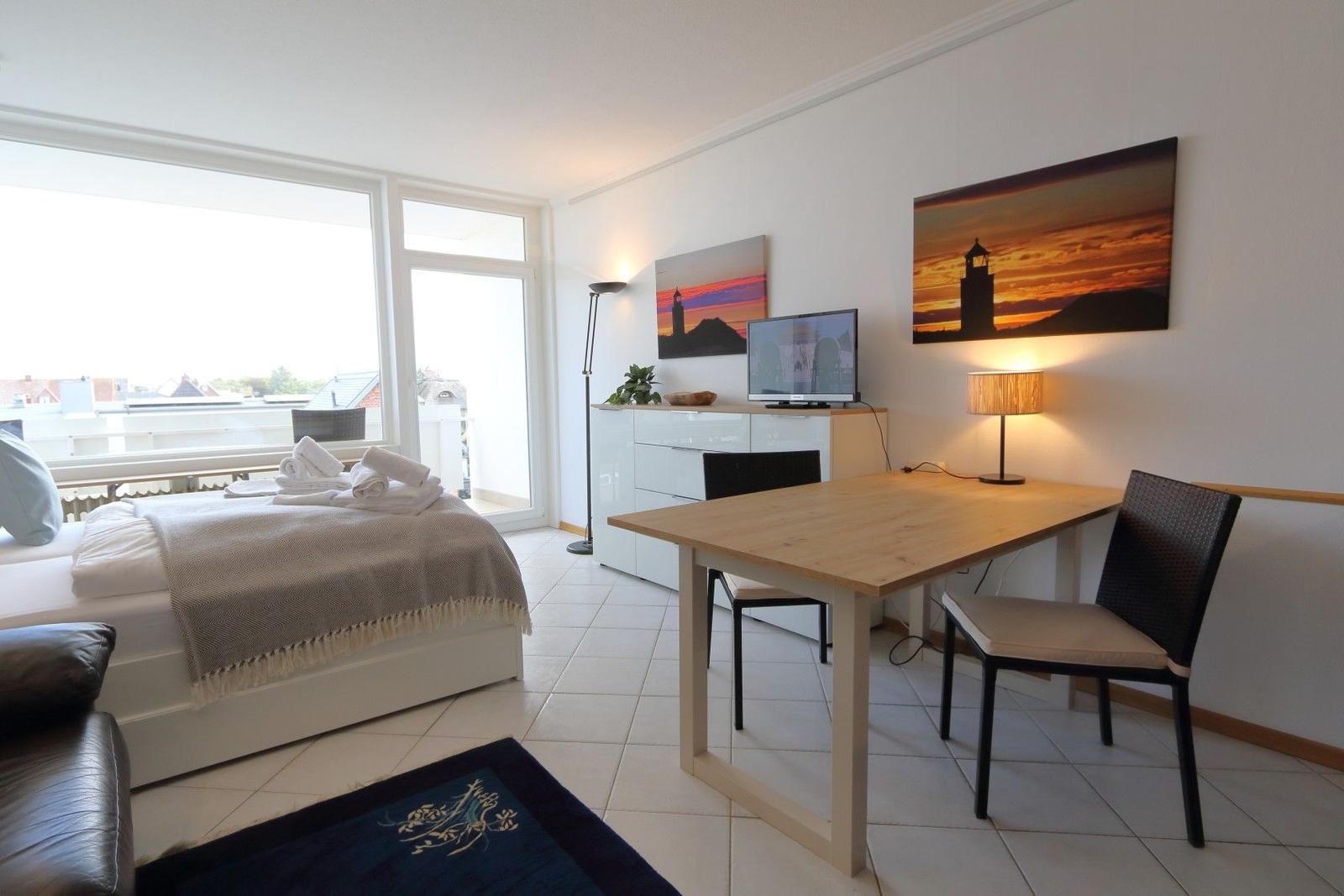 Bedroom with bed, desk, TV, and balcony view.