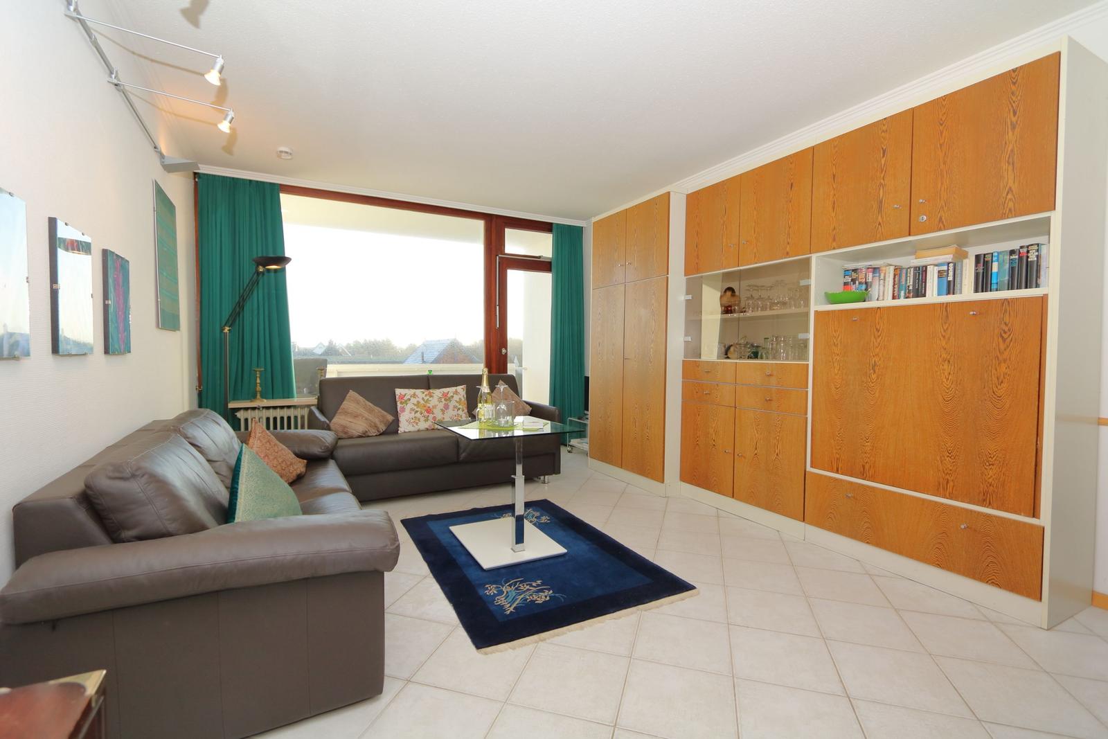 Living room with sofa, coffee table, and wooden cabinet. Large window with view.
