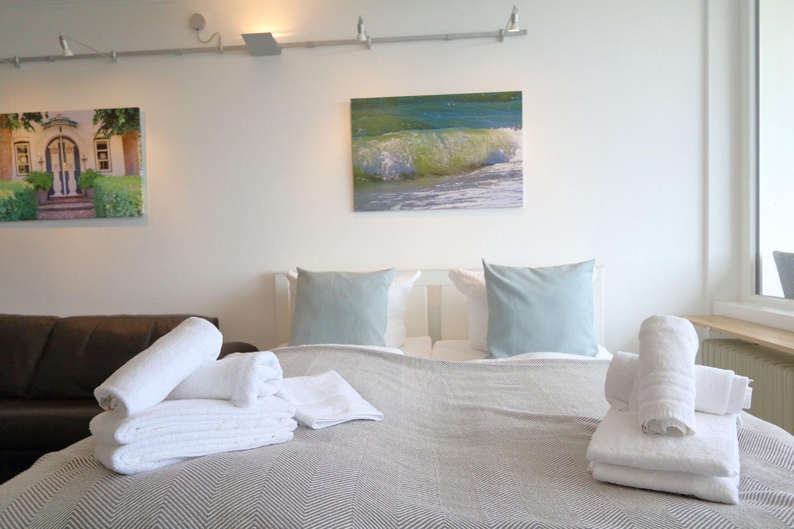 A bed with white pillows and folded towels. Two pictures hang on the wall.