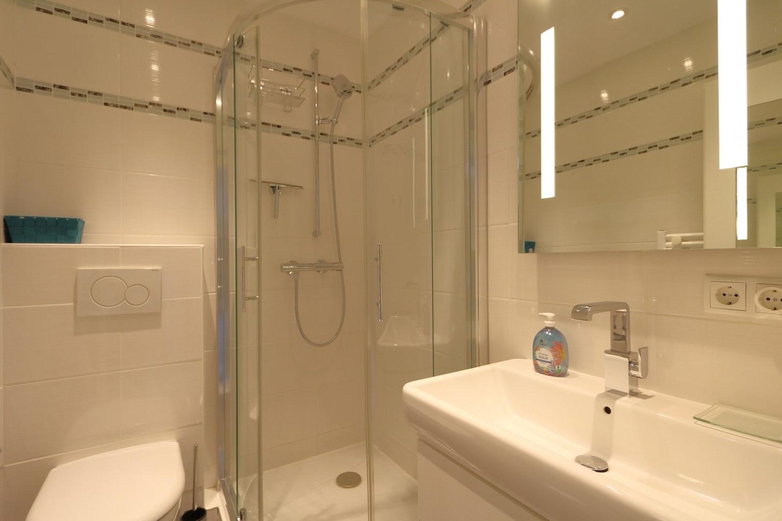 Bathroom with shower, sink and toilet. Tiles and mirror are visible.