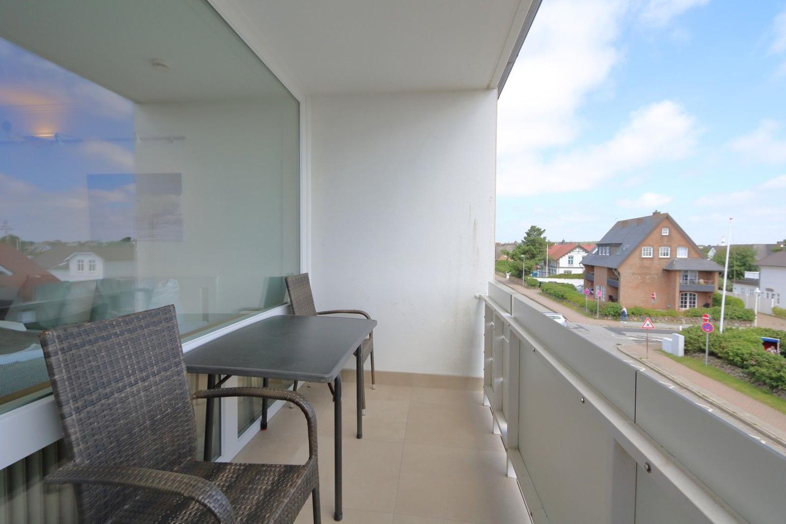 Balcony with table and chairs. View of street and houses.