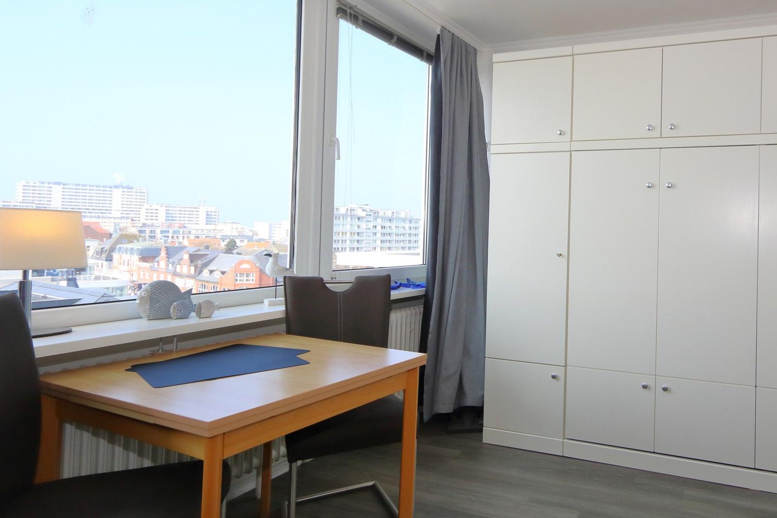 Ein Zimmer mit Schreibtisch, Fenster und weißen Schränken.