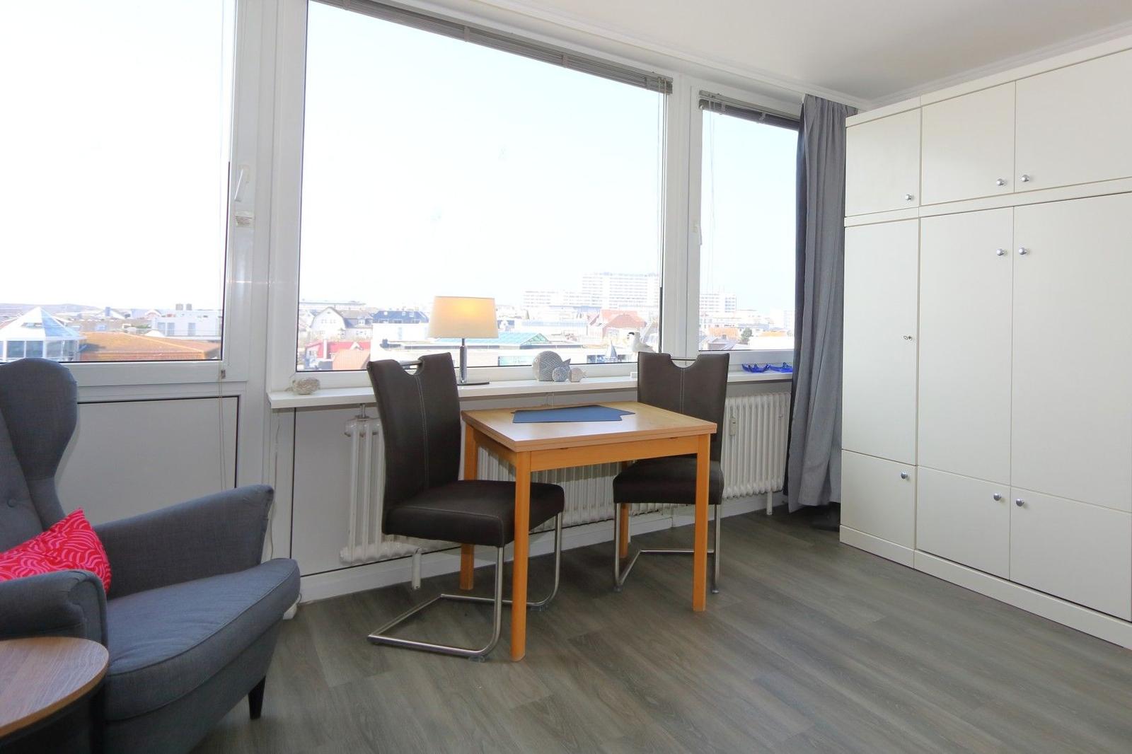 Zimmer mit Tisch, Stühlen, Sessel und großem Fenster mit Blick auf die Stadt.