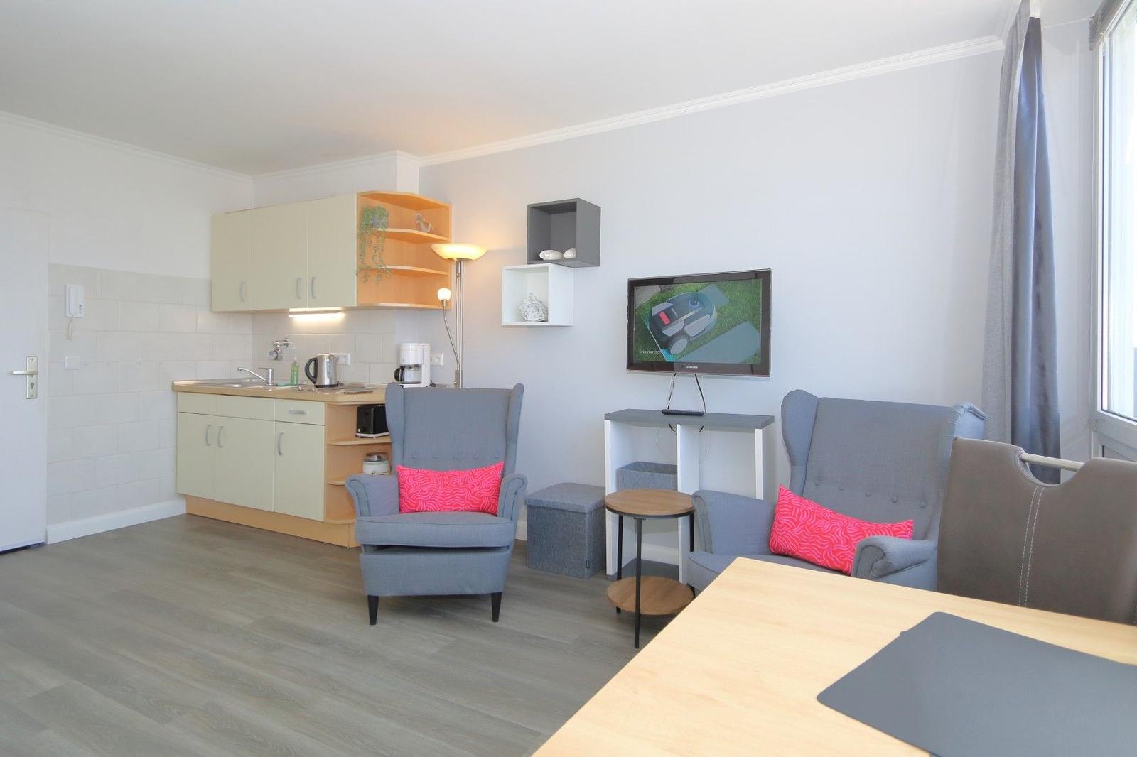 Wohnung mit Küche, zwei Sesseln und Fernseher an der Wand.