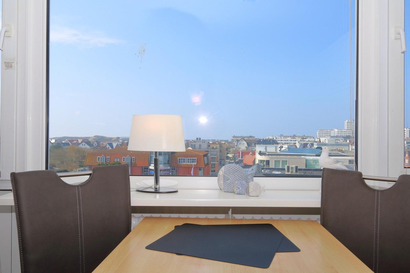 Esstisch mit zwei Stühlen vor großem Fenster mit Stadtblick.
