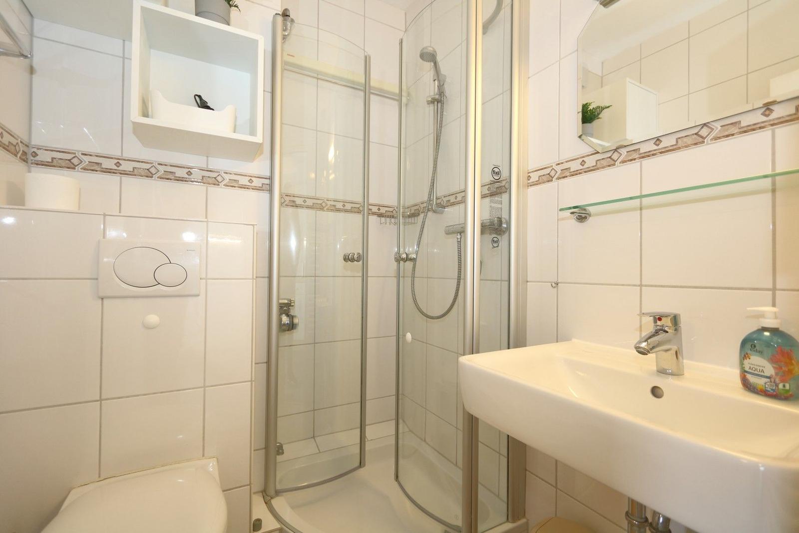 Badezimmer mit Dusche, Waschbecken und Toilette. Fliesenwand mit Mosaikstreifen.
