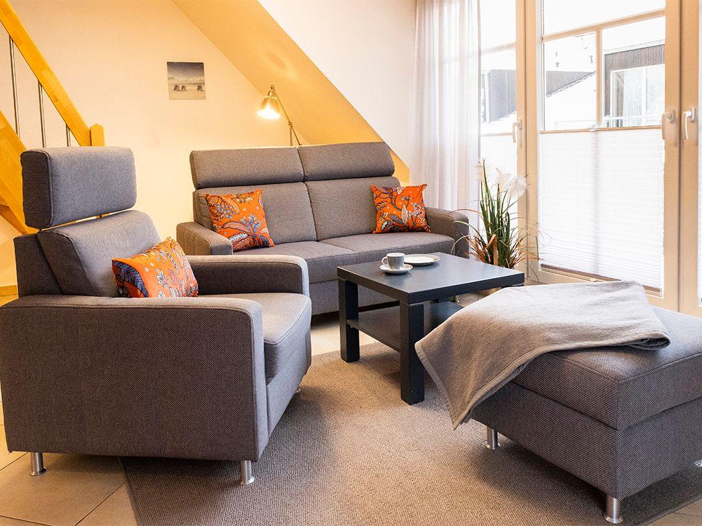 Wohnzimmer mit grauem Sofa, Sessel und Tisch. Fenster mit Jalousien und Pflanze.