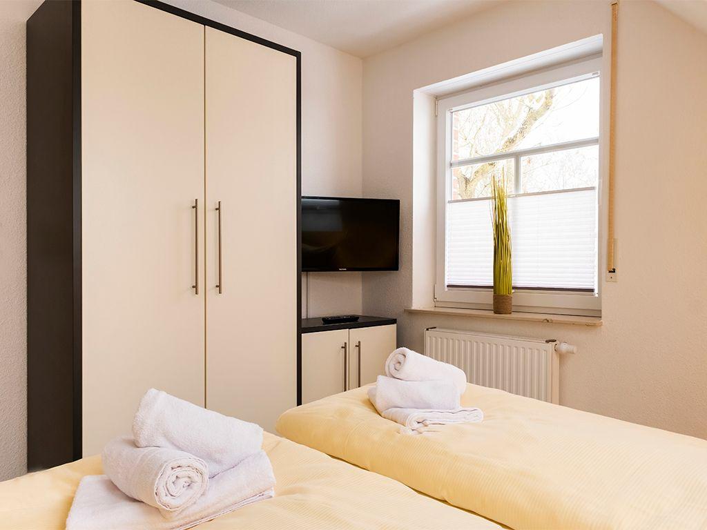 Schlafzimmer mit Bett, Kleiderschrank und TV. Fenster mit Jalousie und Zimmerpflanze.
