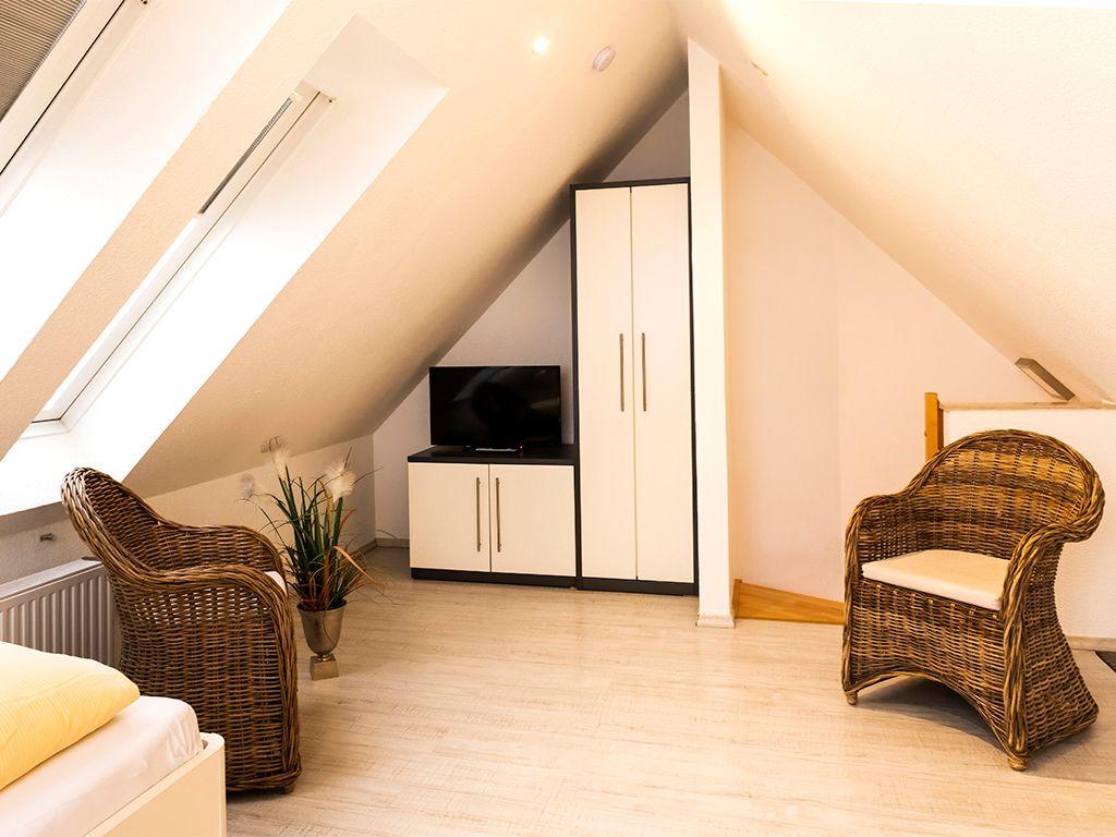 Dachgeschosszimmer mit zwei Rattanstühlen, TV und Schrank unter Dachschrägen.