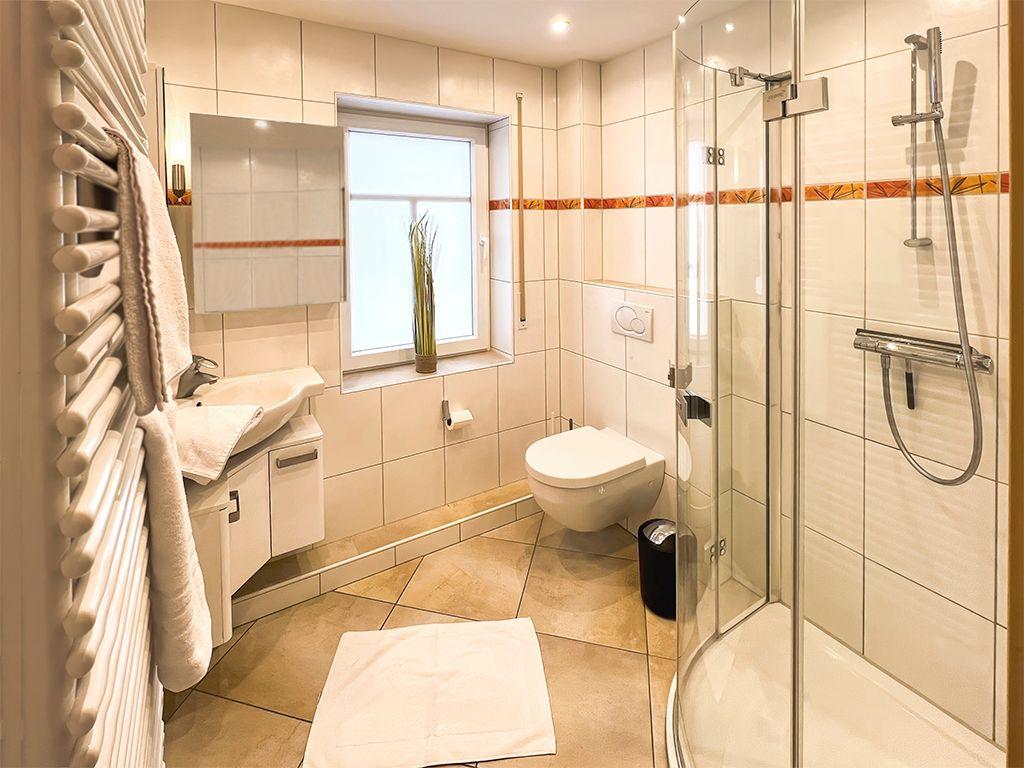 Badezimmer mit Dusche, Waschbecken und Toilette. Fenster mit Pflanze und Handtuchhalter.