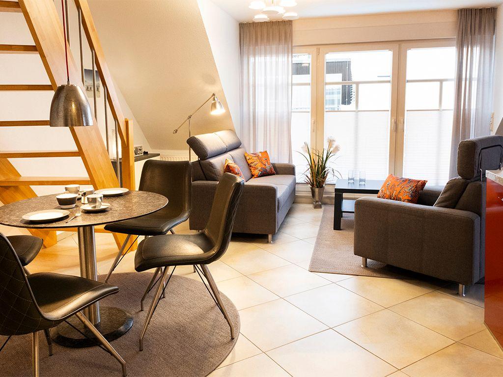 Wohnzimmer mit Sofa, Sessel und Esstisch unter Holztreppe.