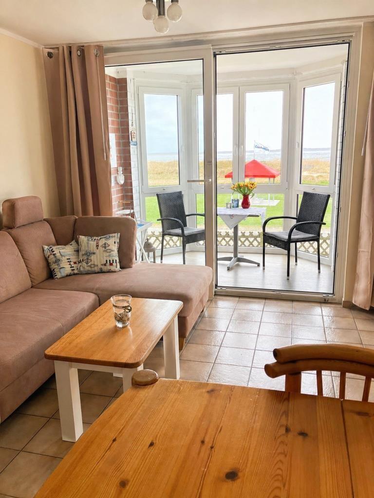 Wohnzimmer mit Sofa, Tisch und Blick auf Terrasse mit Stühlen und Tisch.