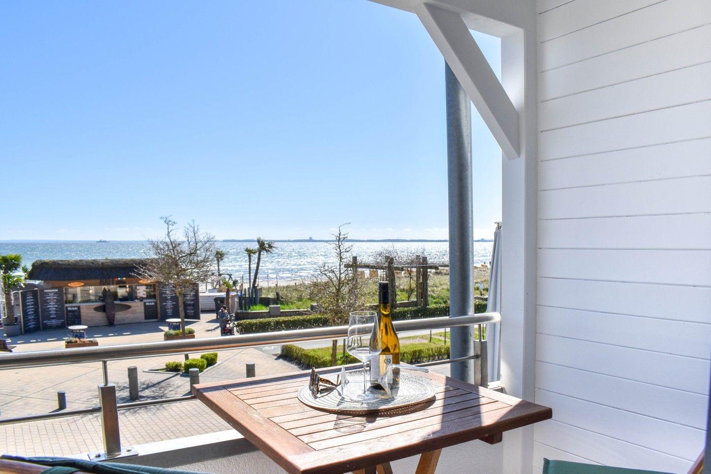 Terrasse mit Tisch, Wein und Meerblick. Hintergrund: Strand und Restaurant.