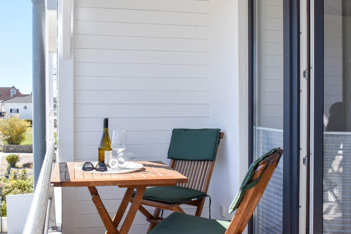 Balkon mit Holztisch, zwei Stühlen und Weinflasche. Blick auf grüne Landschaft.