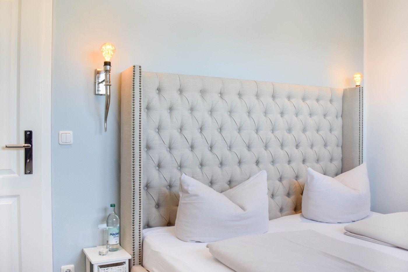 Schlafzimmer mit großem Bett, gepolstertem Kopfteil und Nachttisch mit Flasche.