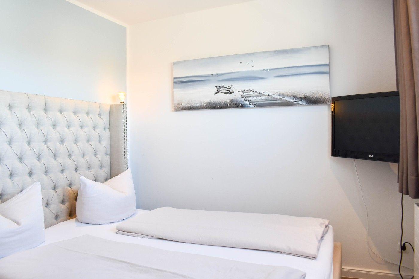 Schlafzimmer mit Bett, Wandbild und Fernseher an der Wand.