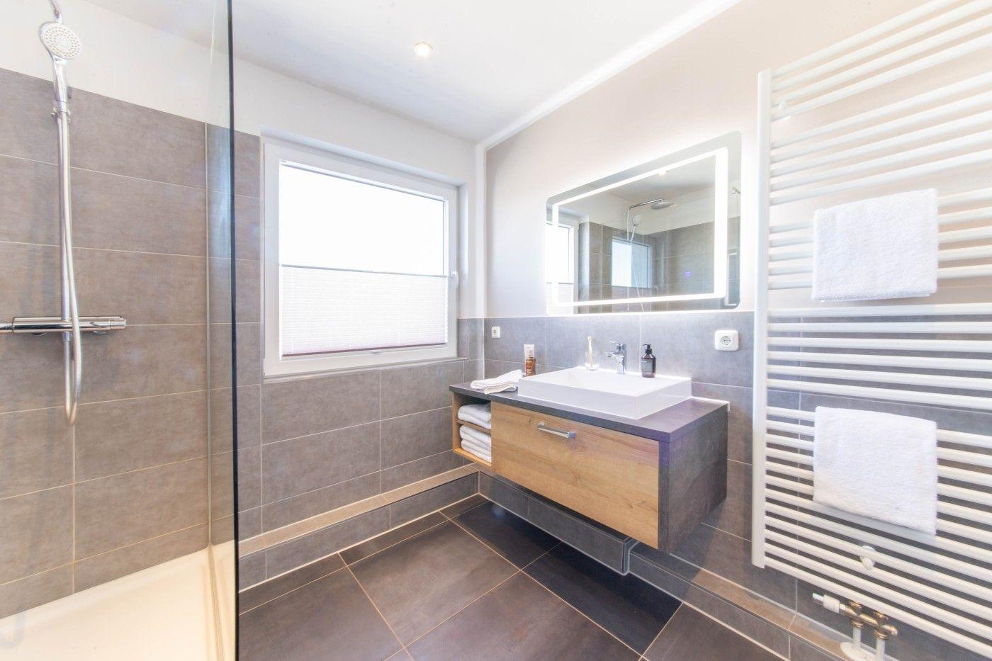 Badezimmer mit Dusche, Waschtisch und Heizkörper. Fenster mit Jalousie.