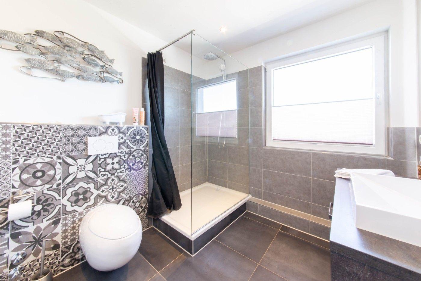 Bad mit Dusche, Waschbecken und Toilette. Wandfliesen mit Muster, Fenster und Duschvorhang.