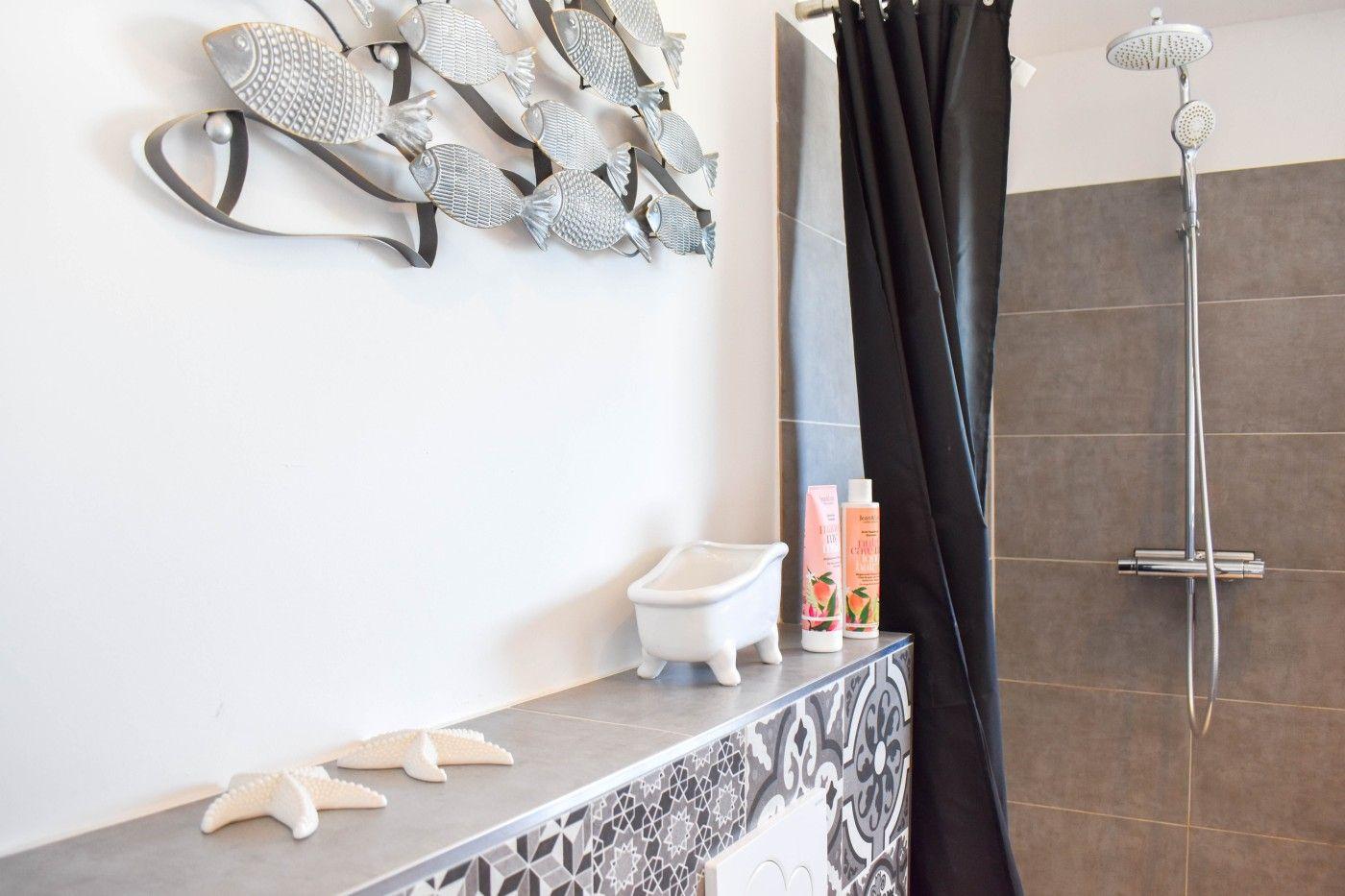 Badezimmer mit Dusche, Duschvorhang und dekorativen Fischfiguren an der Wand.