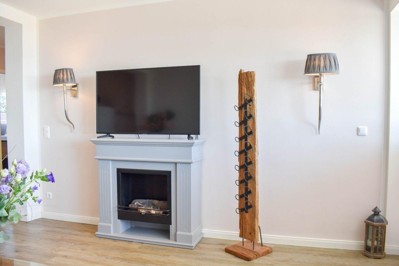Ein Kamin mit Fernseher, Wandlampen und einem Holzweinregal.