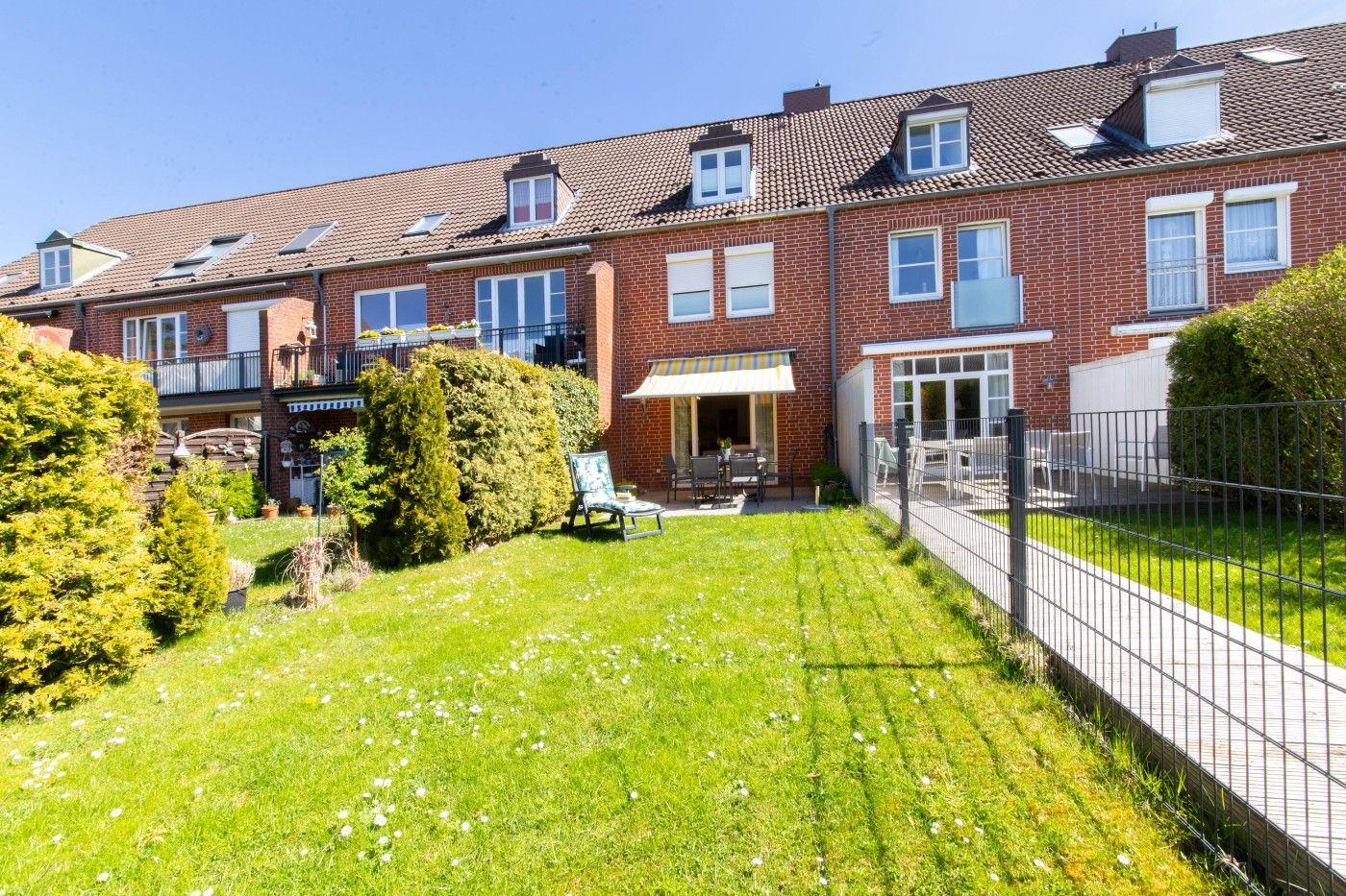Haus mit Garten, Terrasse und Balkon. Grünfläche mit Liegestuhl und Hecke.