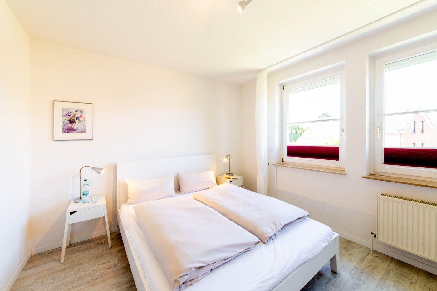 Schlafzimmer mit Doppelbett, zwei Fenstern und Nachttischen.