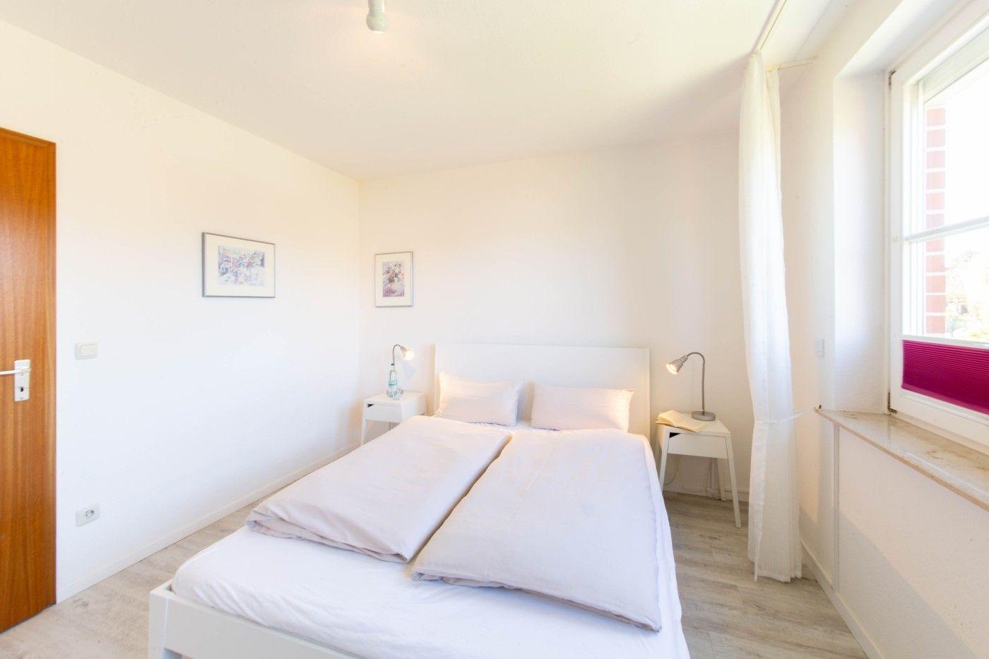 Schlafzimmer mit Doppelbett, zwei Nachttischen und Fenster mit Vorhang.